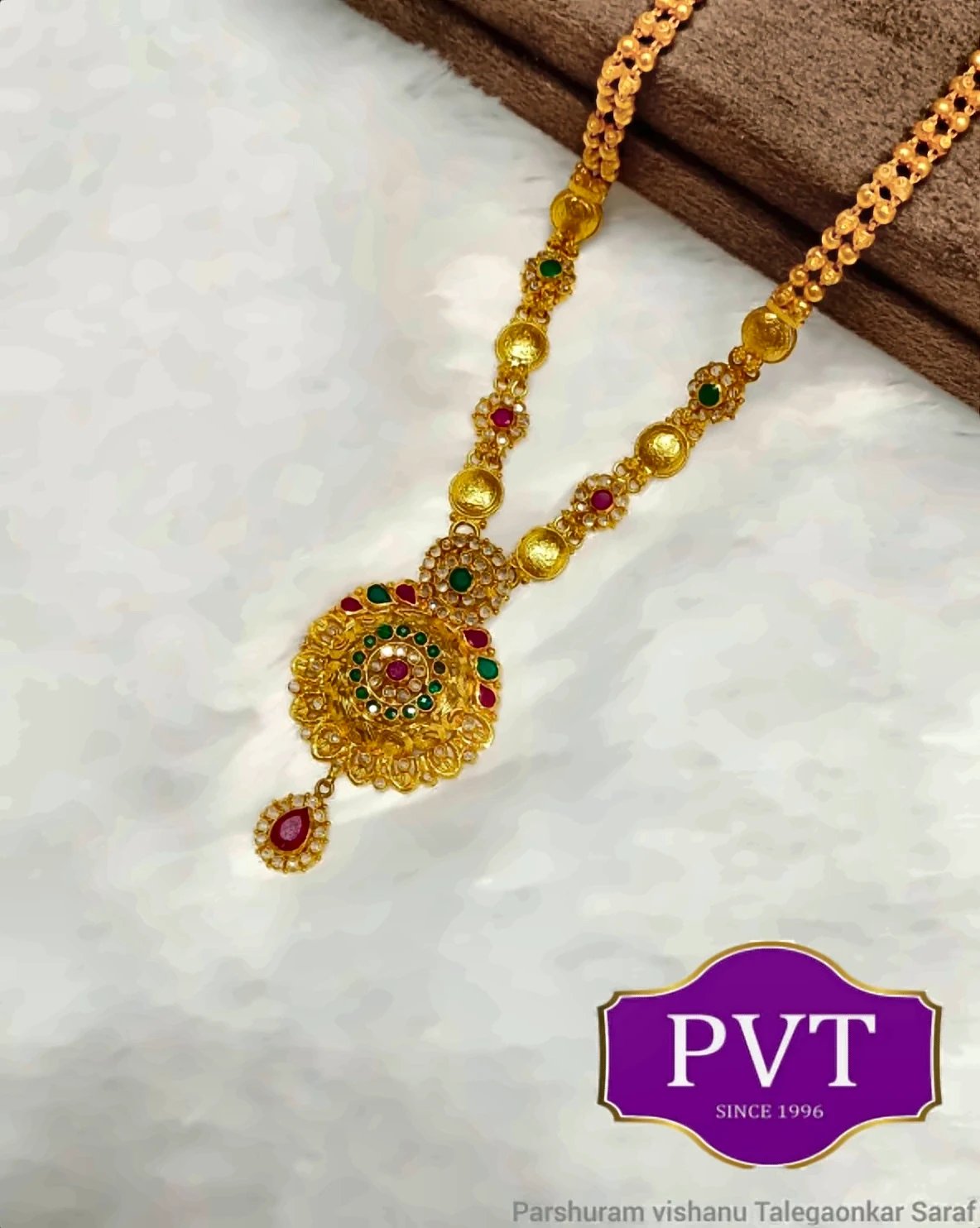 Gold long necklace with red and green stones and a floral medallion pendant